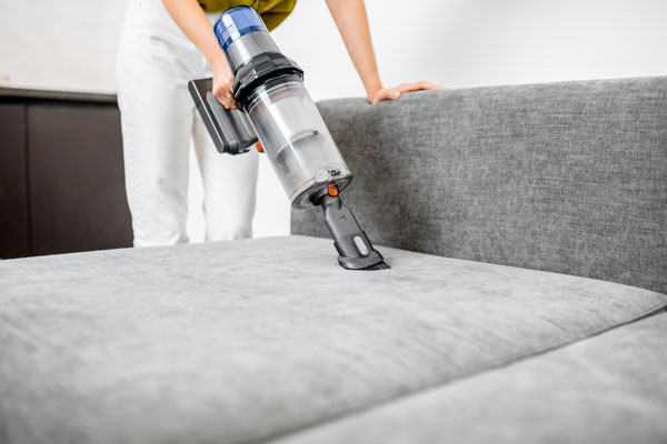 A woman using a portable vacuum cleaner to clean a sofa