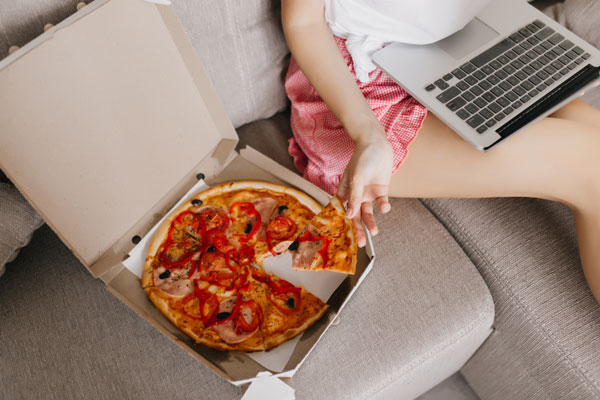 A woman eating pizza on a sofa