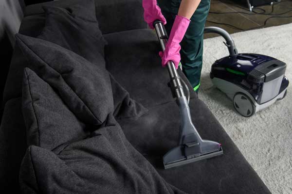 A woman vacuuming a black sofa